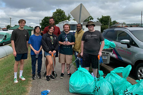 A group of smiling employees from FAST hold trash pickers and stand in front of bags filled with garbage they’ve collected